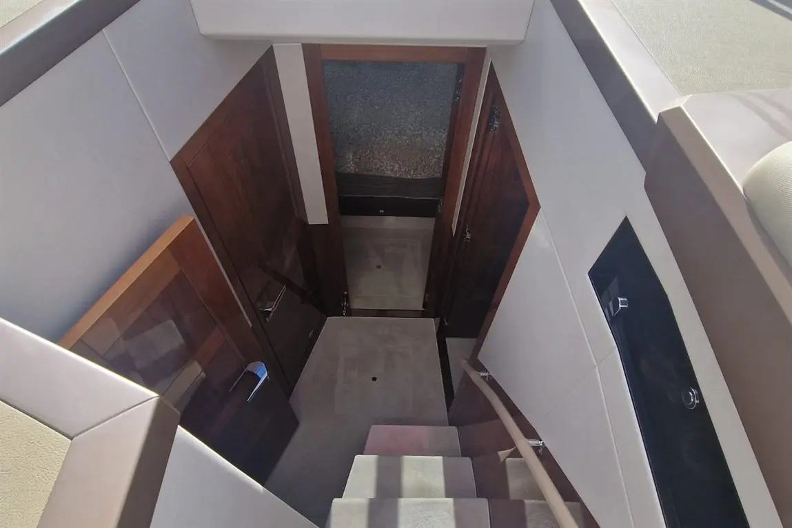 Interior view of a yacht stairway leading down to a hallway with wooden doors and carpeted flooring.